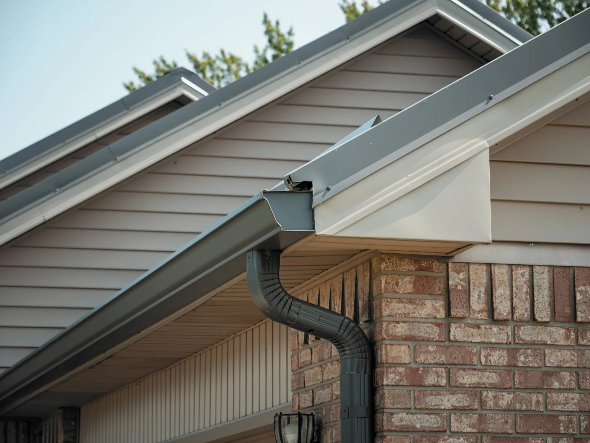 Close view of a seamless aluminum K-style gutter, outlet, and downspout at an eave