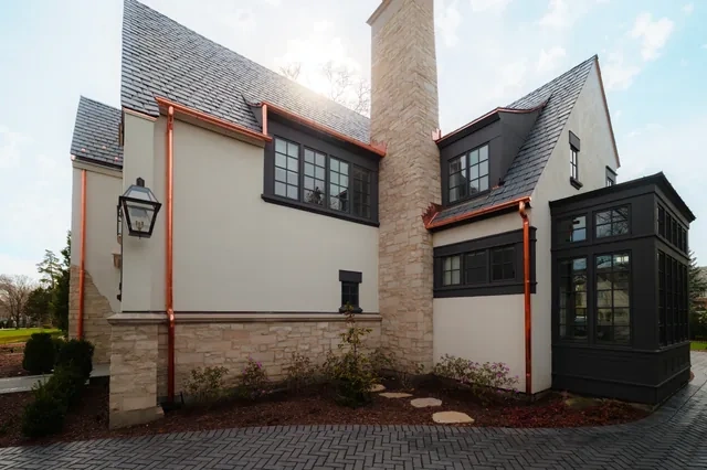 Copper downspout and roof details beside a stone chimney on the Hinsdale residence
