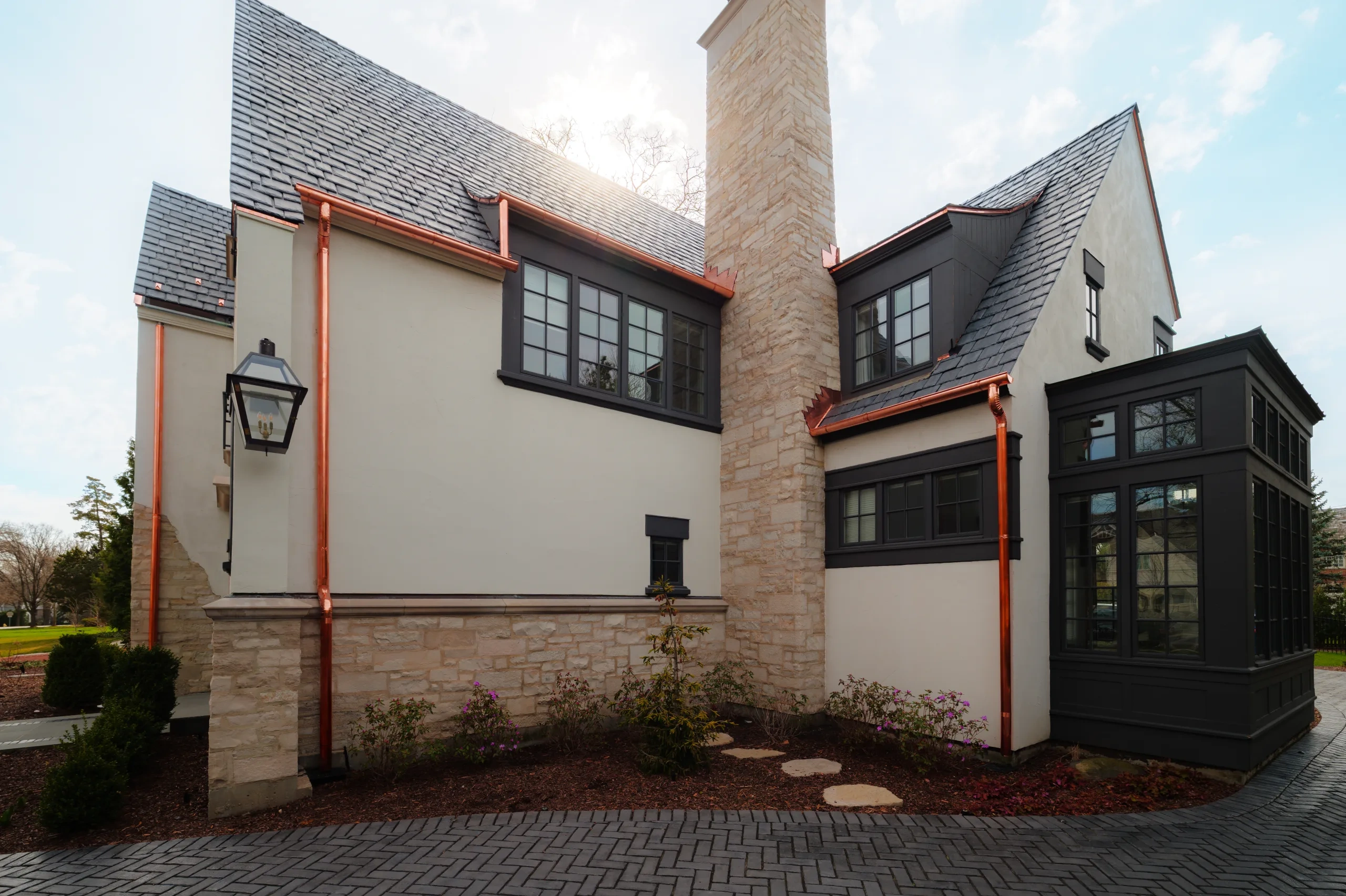 Copper downspouts routed vertically beside masonry and connected to upper roof drainage