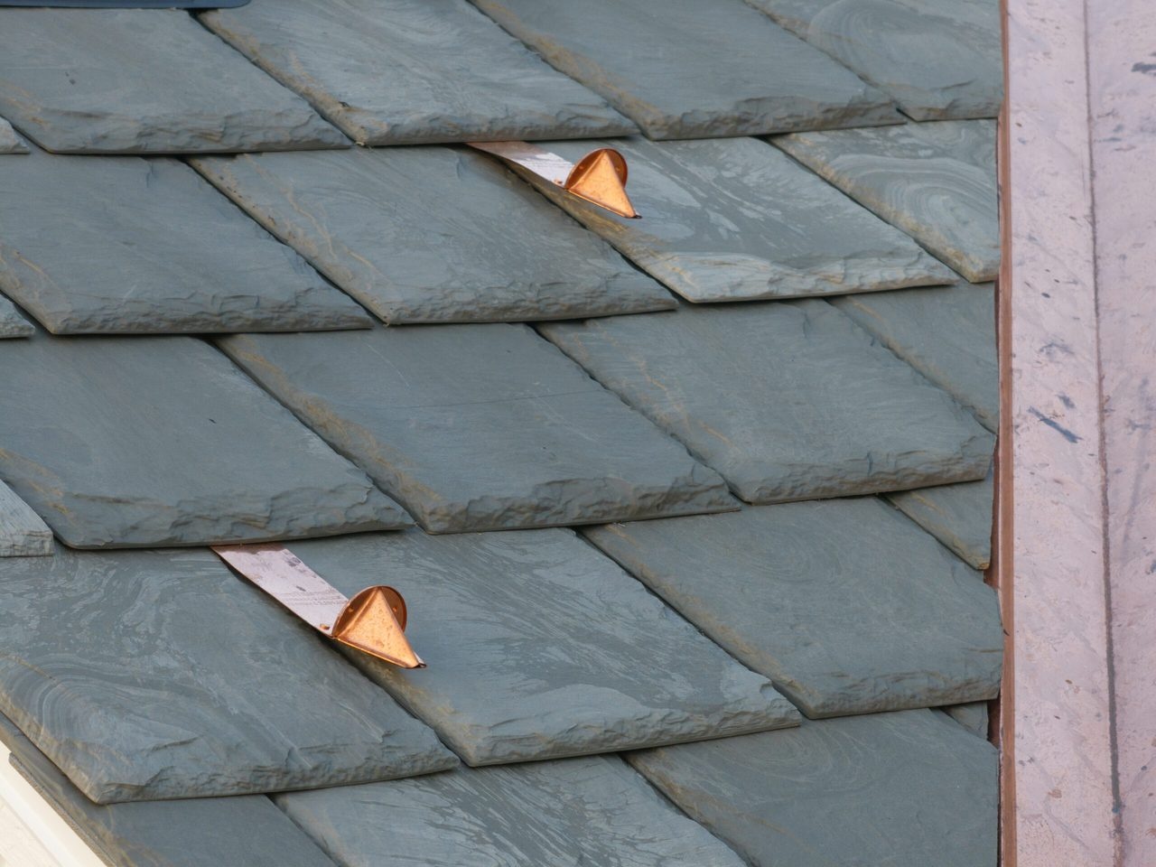 Close view of staggered slate-profile roof courses and copper detailing