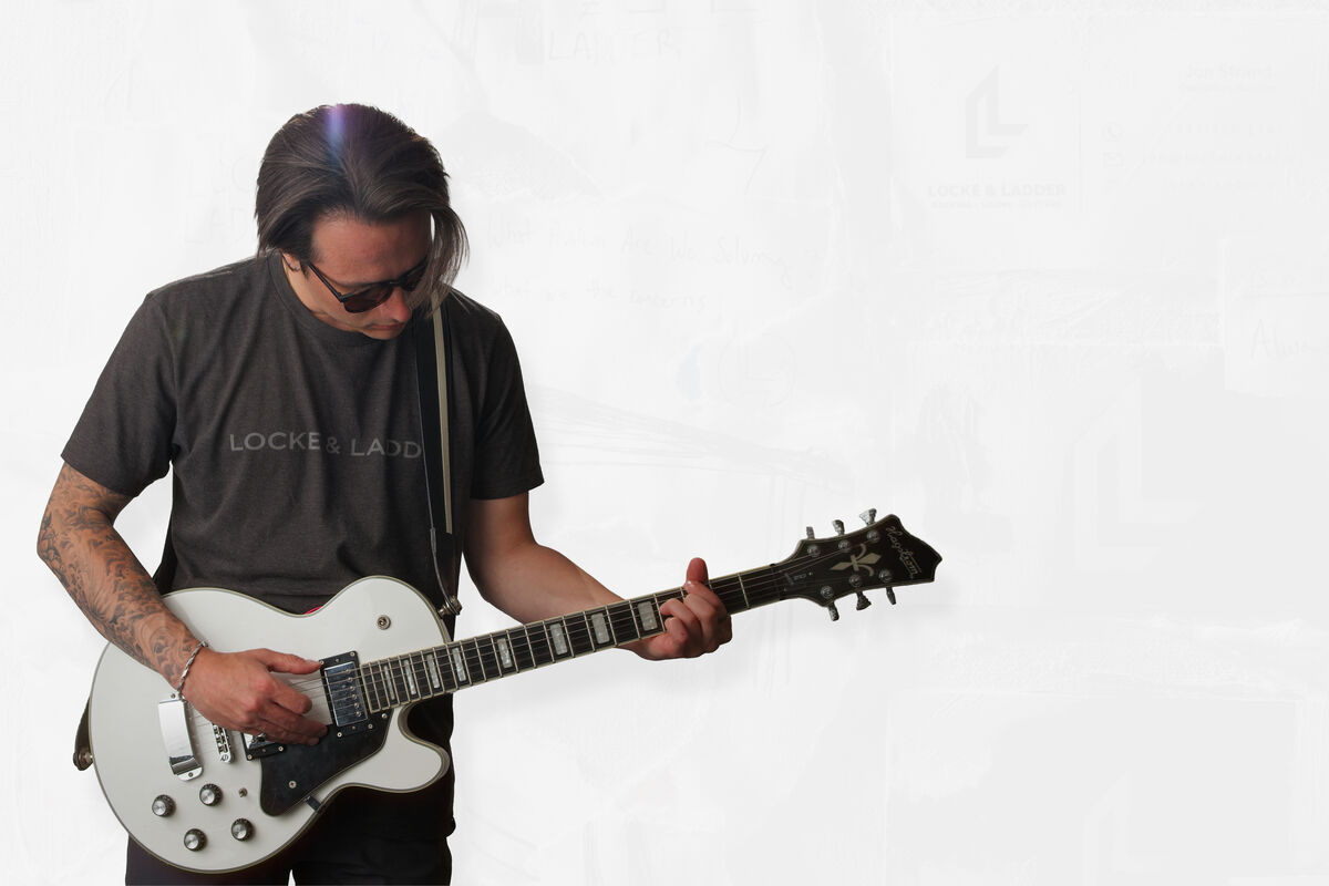 Locke & Ladder team member playing a white electric guitar against a white studio backdrop