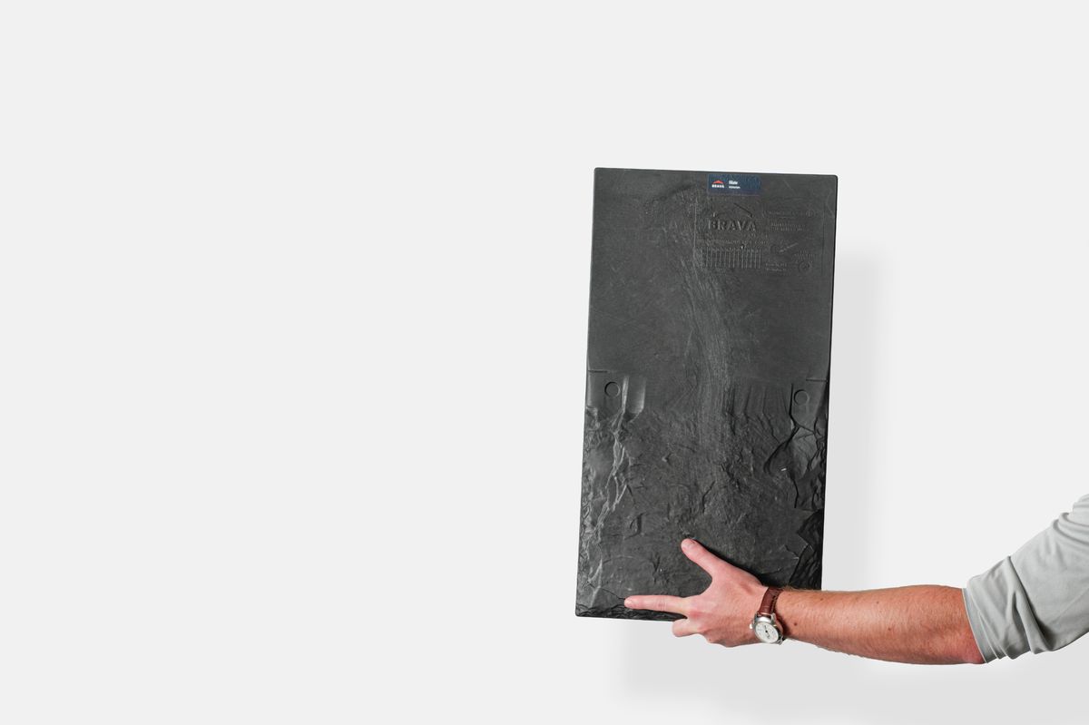 Hand presenting a Brava synthetic slate roofing panel against a white studio wall