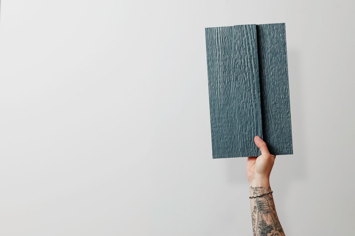 Hand holding up dark woodgrain siding sample boards against a white studio wall